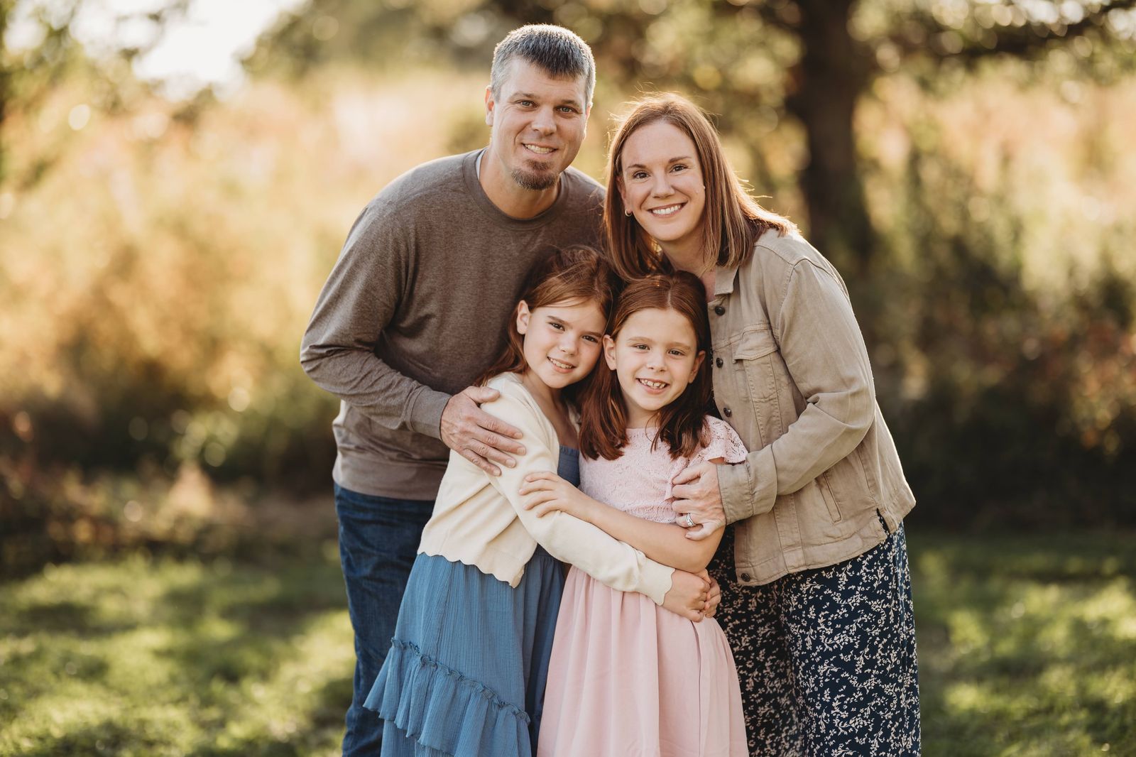 Sarah with her husband and their two daughters, outdoors in golden light